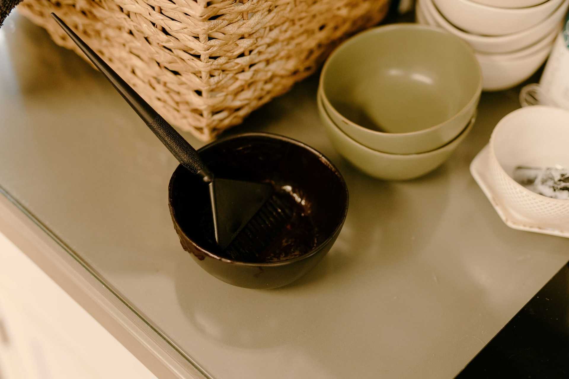 Hair dye bowl and brush on a gray countertop, with other bowls nearby.
