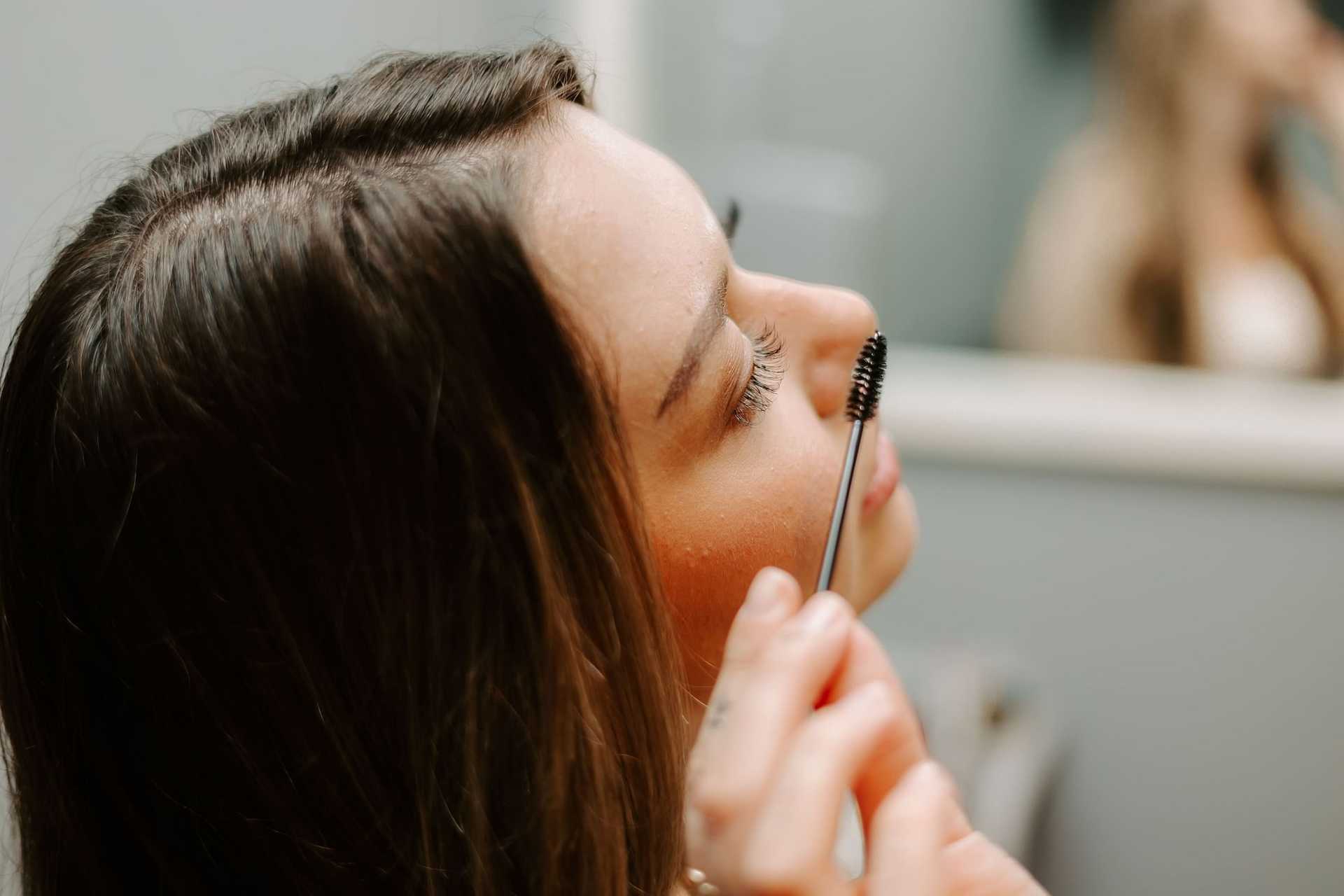 Woman applying mascara in front of a mirror.