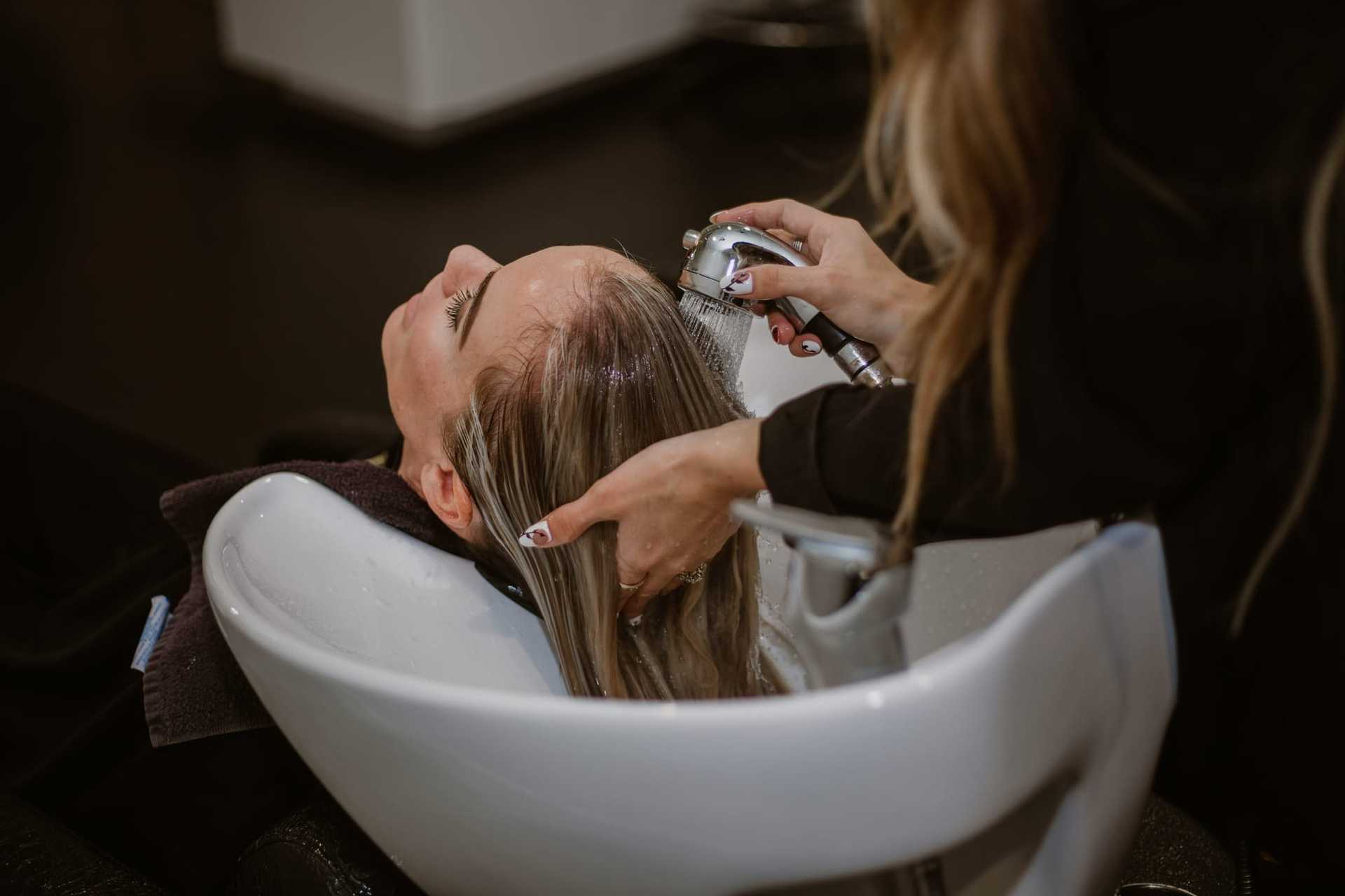 Hairdresser washing client's hair in a salon sink.